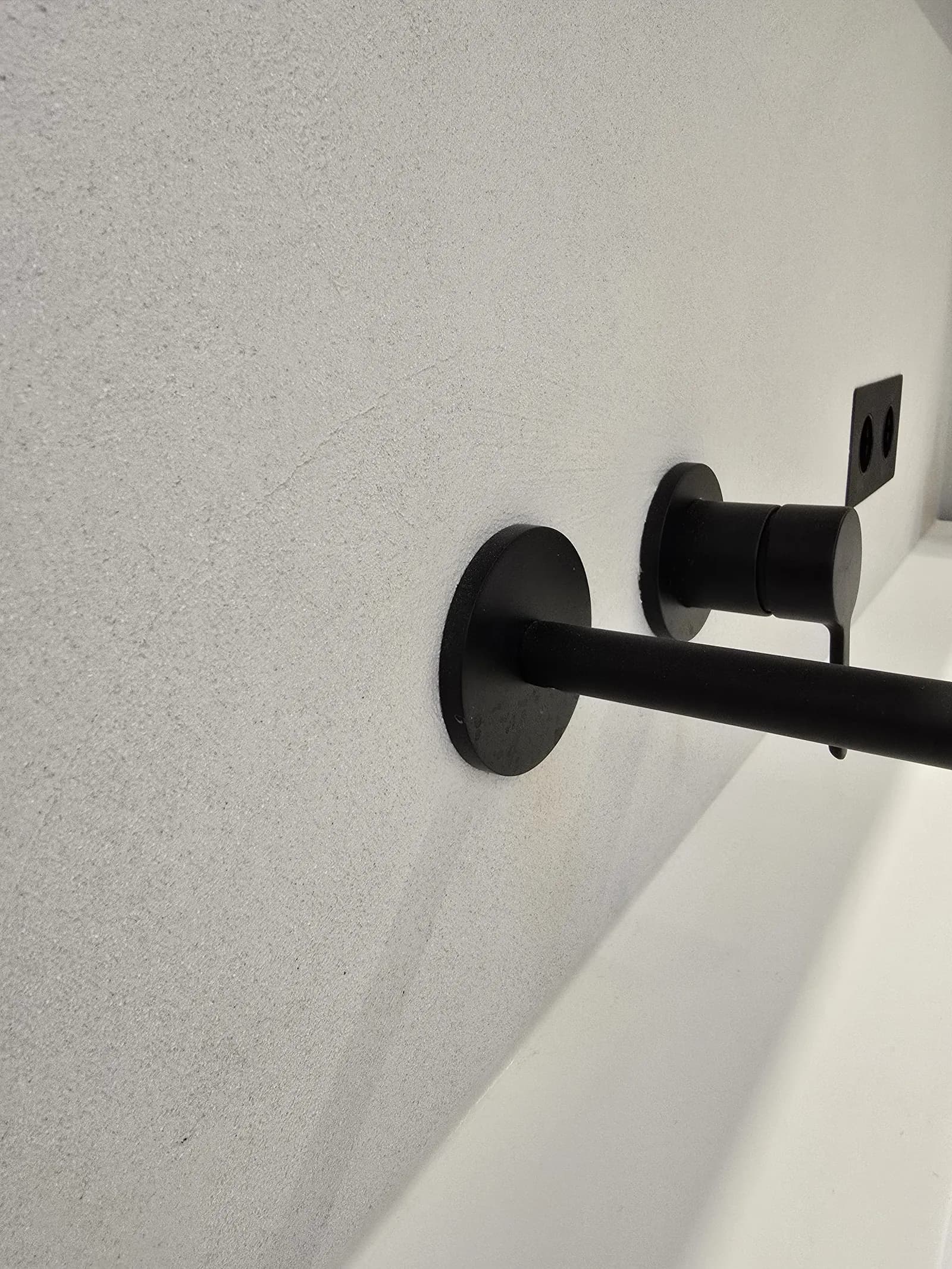 Detail einer fugenlosen Wand mit schwarzer Armatur